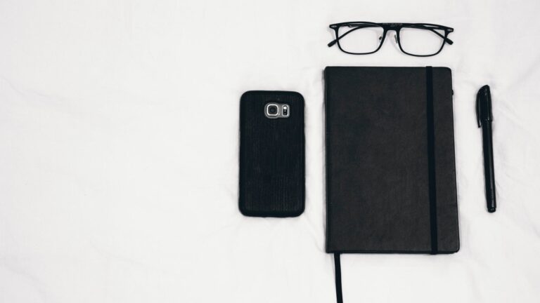 black smartphone beside planner and eyeglasses and pen