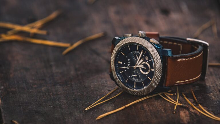 round silver colored fossil chronograph watch with brown leather band on brown wooden surface